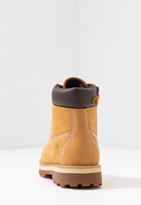Bottine en daim beige avec un col en cuir marron, présentant des coutures blanches et une semelle en caoutchouc texturée. La vue arrière met en avant le détail du logo.
