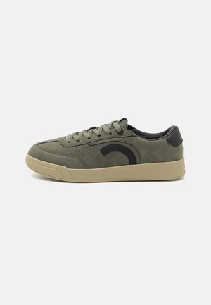 Baskets basses vert olive avec semelle en caoutchouc beige, patch noir au talon, motif courbé noir sur le côté et fermeture à lacets.