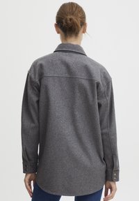 Szara wełniana koszula z kołnierzykiem, długimi rękawami i mankietami na guziki. Charakteryzuje się prostym dołem i luźnym krojem z tyłu.