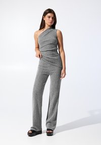 Grå ensidet jumpsuit med et teksturet mønster, tætsiddende liv, vide bukser og sorte platform sandaler med en glat stofoverflade.