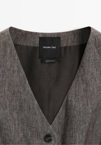 Veste marron texturée avec bouton noir et étiquette noire portant la mention Massimo Dutti, fabriquée au Maroc, à l'intérieur du col.