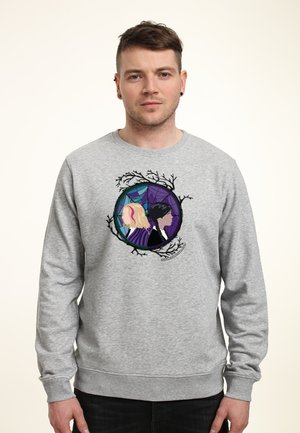 Man wearing gray sweatshirt with graphic of two women back-to-back inside circular frame with branches and spiderweb design.