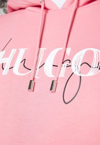 Felpa rosa con logo stilizzato "HUGO" in bianco e nero e cordini rosa con puntali metallici argentati.