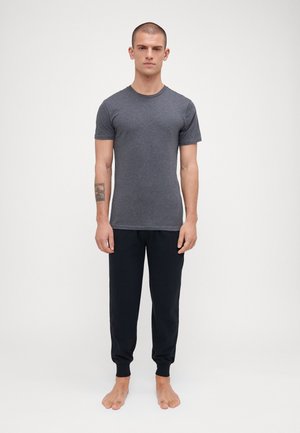 Grå kortærmet t-shirt i slank pasform, parret med sorte sweatpants med ribkanter ved anklerne. Modellen står barfodet og oprejst.
