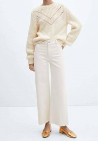 Suéter de lana color crema con un patrón geométrico, combinado con unos pantalones de mezclilla de pierna ancha en beige claro y bailarinas doradas con un detalle de lazo.