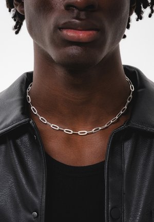 Silver chain necklace made of elongated links, resting on a dark fabric shirt, against a smooth background.