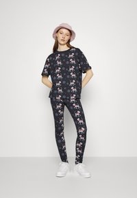 Conjunto de pijama preto com padrões de renas e flocos de neve. Tecido suave, camisa de mangas curtas e leggings justas. Ténis brancos incluídos.