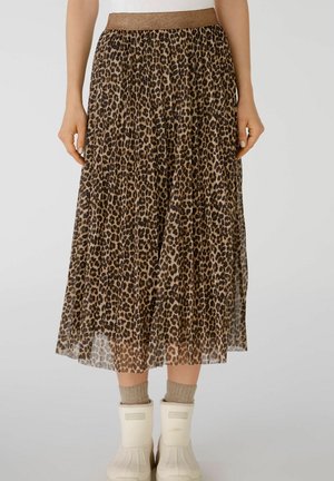 Leopardenmuster plissierter Midirock mit einem metallischen Taillenbund, getragen mit beigen Socken und weißen Stiefeletten auf hellem Hintergrund.