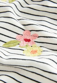 Tissu blanc à rayures horizontales noires avec des fleurs brodées roses et jaunes et des feuilles vertes.