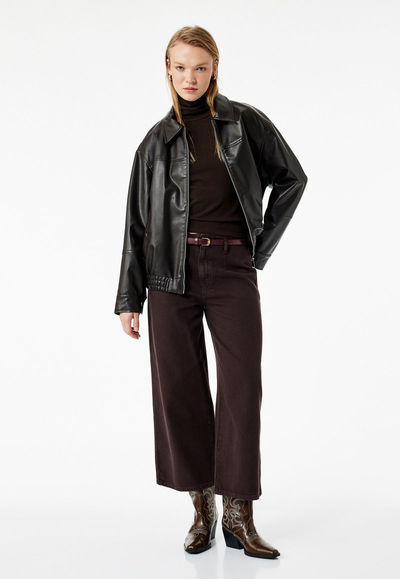 Schwarze Lederjacke über einem braunen Rollkragenpullover, kombiniert mit weit geschnittenen bordeauxroten Hosen und braunen bestickten Cowboy-Stiefeln.