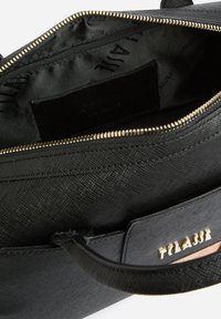 Borsa nera texturizzata con cerniera dorata, vista dall'alto aperta che mostra la fodera interna in tessuto nero con una piccola tasca con zip.