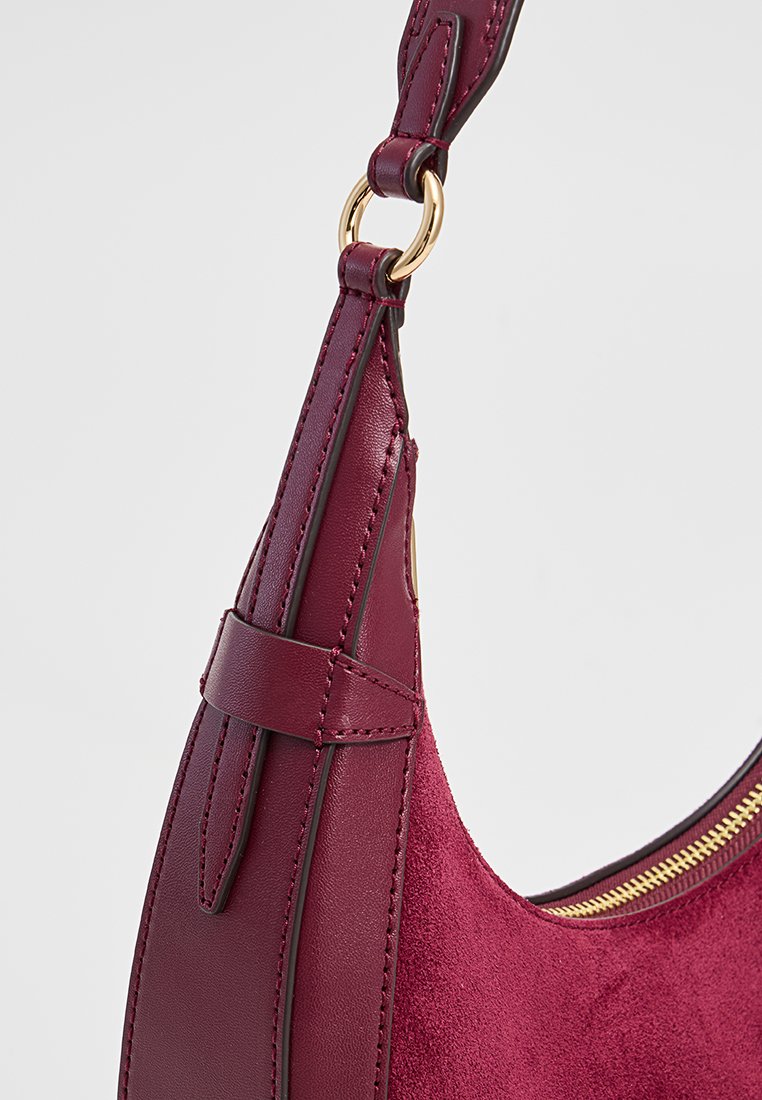 Sac à épaule en cuir bordeaux et en daim avec une fermeture éclair dorée, une sangle réglable et un fond plat pour plus de stabilité. Design minimaliste avec des lignes épurées.