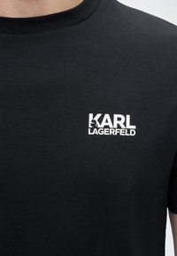 Μαύρο T-shirt με λευκό λογότυπο "KARL LAGERFELD" στο αριστερό στήθος, με ένα μικρό γραφικό σιλουέτας μέσα στο γράμμα K.
