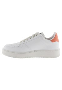 Zapatilla baja blanca con cordones beige y una tira en el talón de color coral naranja, que presenta una suela gruesa y texturizada y una área de puntera perforada.