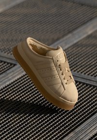 Beige alacsony szárú sneakers, sima anyagból, három csíkkal, kerek orral és texturált gumi talppal.