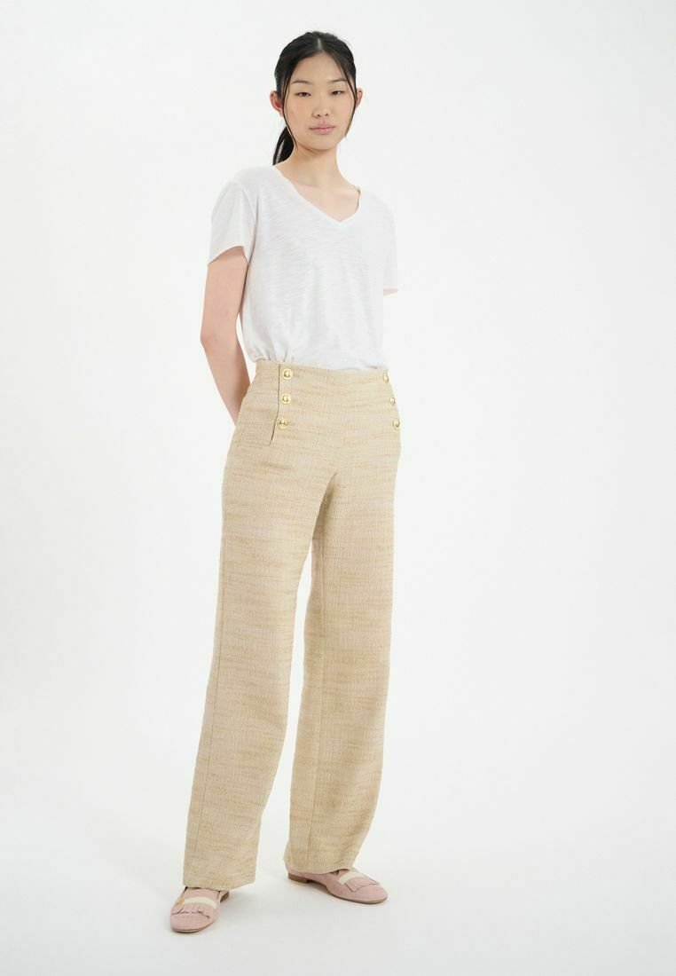 Pantalon large beige en tissu texturé, avec des accents de boutons dorés à la taille. Assorti à un t-shirt à col en V blanc uni.