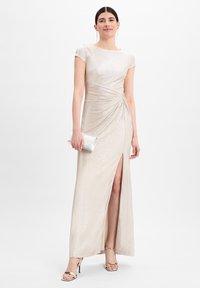 Langes, elfenbeinfarbenes Abendkleid aus glänzendem Stoff, mit kurzen Ärmeln, Raffung an der Taille und einem Schlitz bis zum Oberschenkel. Begleitet von einer silbernen Clutch.