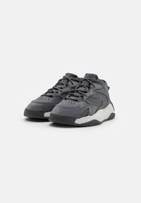 Grå sneakers i mocka och mesh med en tjock vit sula, utrustade med snörning, strukturerade paneler och en gummiyttersula.