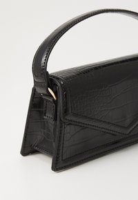 Sac à main noir en cuir synthétique avec une texture crocodile, un design angulaire, une forme structurée et une anse incurvée. Accents de quincaillerie dorée inclus.