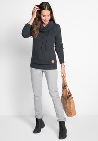 Maglione lavorato a maglia grigio scuro con collo a cowl e lacci, polsini e orlo a coste; abbinato a pantaloni grigio chiaro e stivali neri con lacci.