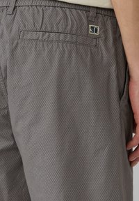 Grau gemusterte Shorts aus leichtem Stoff, mit einer Gesäßtasche und einem gestickten Logo in der oberen Ecke. Glatte Textur.
