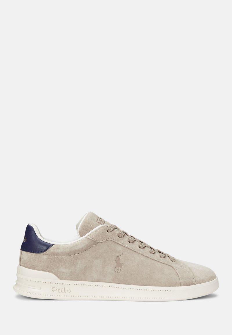 Beige suede sneaker with a smooth texture, white rubber sole, dark blue heel accent, and tonal logo on the side. Lace-up design.