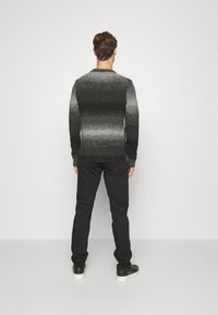 Grå ombre genser med ribbestrikket kant og mansjetter, kombinert med svarte bukser og svarte joggesko, sett fra baksiden mot en hvit bakgrunn.