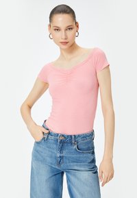 Top corto a maniche corte di colore rosa con scollatura bordata di pizzo e dettagli arricciati, abbinato a jeans in denim blu a vita alta.