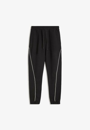 Pantaloni de trening negri cu un cordon la talie, cu dungi albe pe laterale și manșete elastice la glezne. Realizați dintr-un material moale și texturat.