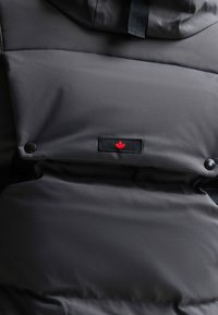 Must mustakate isolatsiooni jakk, millel on sile matt viimistlus. Omab punase vahtrapleki logo, nööpe ja tekstuuriga kapuutsi.