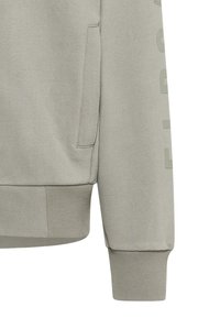 Hellgrauer Pullover mit strukturierter Stoffoberfläche, gerippten Bündchen und Saum sowie einer Seitentasche. Dezente Schriftzüge entlang des Ärmels.