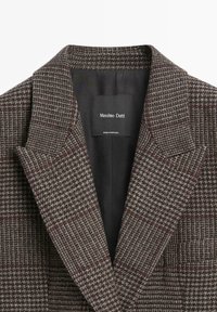 Blazer a quadri marrone con revers a punte, realizzato in tessuto texture. Presenta una fodera interna nera e un'etichetta del marchio cucita.