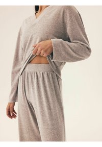 Szary zestaw odzieży domowej składający się z klasycznej bluzki z dekoltem w serek i długimi rękawami oraz spodni z elastycznym paskiem. Gładka tekstura z luźnym krojem.