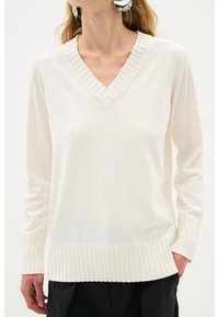 V-Ausschnitt-Pullover in Creme, mit geripptem Kragen und Bündchen. Hergestellt aus weichem Material mit lockerem Schnitt und subtiler Textur.