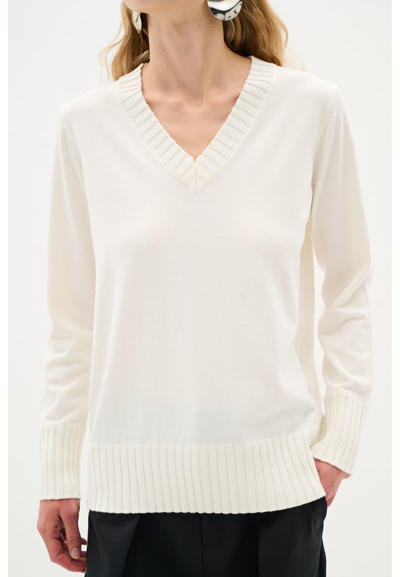 V-Ausschnitt-Pullover in Creme, mit geripptem Kragen und Bündchen. Hergestellt aus weichem Material mit lockerem Schnitt und subtiler Textur.