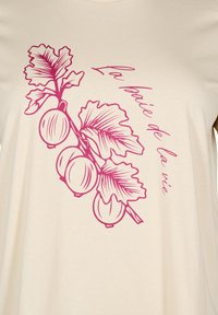Beige t-shirt with a pink illustration of leaves and berries. Text in pink reads "La baie de la vie," featuring soft, smooth fabric.