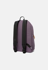 Lila ryggsäck med svarta remmar, som har en slät yta, en sidoficka och ett handtag upptill för enkel transport. Justerbara spännen är synliga.