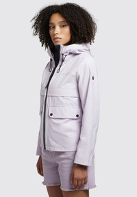 Jacket impermeabilă de culoare violet deschis, cu glugă, fermoar frontal, două buzunare pe piept și sireturi ajustabile. Purtați cu pantaloni scurți asortați.