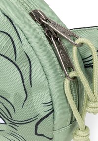 Vihreä kuvioitu pussukka, joka on valmistettu kangasta, jossa on teksturoitu pinta ja vetoketjukiinnitys. Pussukassa on hymyilevä sarjakuvakasvo ja solmittu vetoketjun vetosolu.