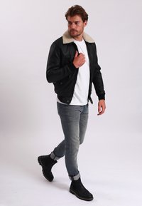 Černá kožená bunda s béžovým kožešinovým límcem, bílým tričkem, světle modrými džínami a černými kotníkovými botami. Modelka jde.