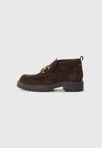 Bottes de cheville en daim marron avec une épaisse semelle en caoutchouc noir, dotées d'un détail de sangle en métal doré décoratif et d'une languette à l'arrière.