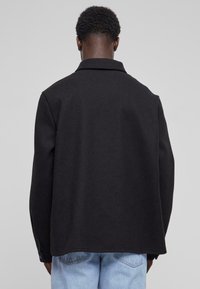 Zwarte wollen jas met een kraag, met een relaxed fit en een soepele textuur. De achterkant heeft minimale details en een casual stijl met blauwe spijkerbroeken.