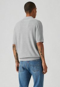 Grå kortärmad tröja med ribbad nederkant och ärmslut, tillsammans med blå jeans. Tröjan har en enkel, strukturerad yta.