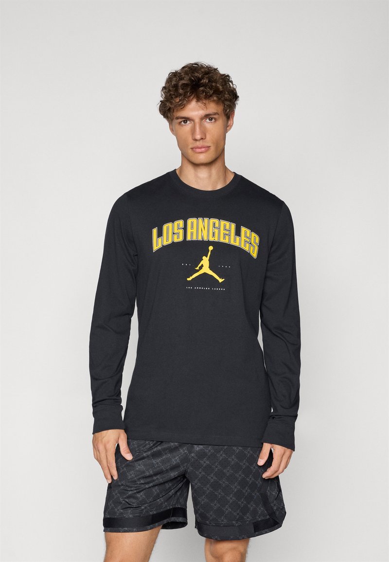 Sort langærmet skjorte med gul "LOS ANGELES" tryk og Jumpman-logo; parret med sorte mønstrede shorts. 100% bomuldsmateriale, afslappet pasform.