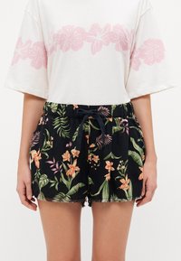 Shorts noirs à motifs floraux avec une taille à cordon, présentant des motifs tropicaux vibrants en orange, rose et vert. Détail de l'ourlet effiloché.