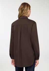 Camicia marrone a maniche lunghe con colletto classico, pieghe sul retro, polsini con bottoni e orlo arrotondato, realizzata in tessuto liscio e leggero.