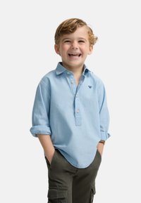 Camisa de algodón de manga larga en azul claro con collar abotonado y mangas remangadas, que presenta un pequeño logotipo bordado en el pecho.