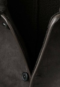 Cappotto in suede marrone con un interno testurizzato, caratterizzato da un ampio colletto, un unico bottone nero e un dettaglio con tasca verticale.