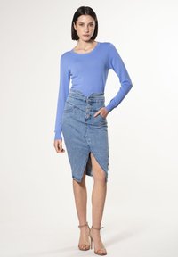 Lichtblauw langemmouwtop gecombineerd met een hooggetailleerde denimrok met een knoopsluiting aan de voorkant, een zijslit en een licht gegolfde tailleband.