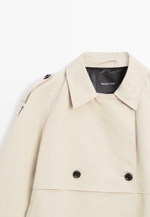 Beiger Trenchcoat mit Kragen, schwarzen Knöpfen vorne und Schulterklappe, schwarzem Innenetikett mit dem Schriftzug "Massimo Dutti".